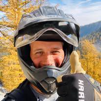 Person wearing motorcycle helmet giving thumbs up in autumn scene.