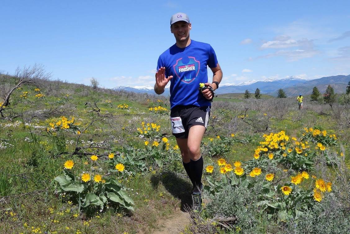 Trail runner in blue shirt on a spring field of yellow flowers under blue sky