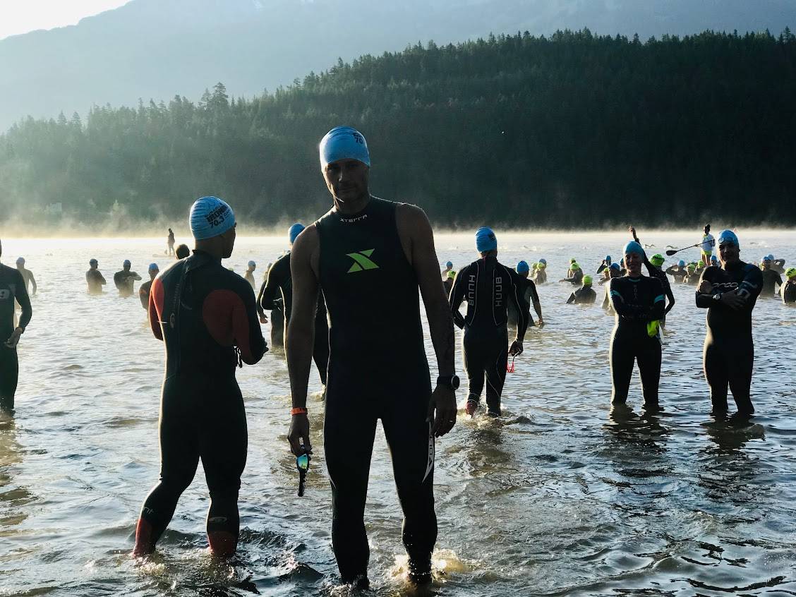 Open-water swimmers in wetsuits at the shore with blue caps.