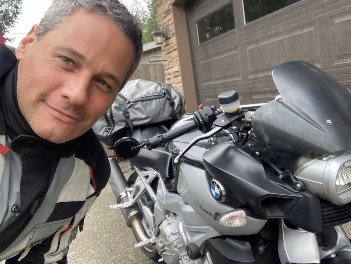 Portrait of a man in motorcycle gear next to a silver BMW sport touring motorcycle