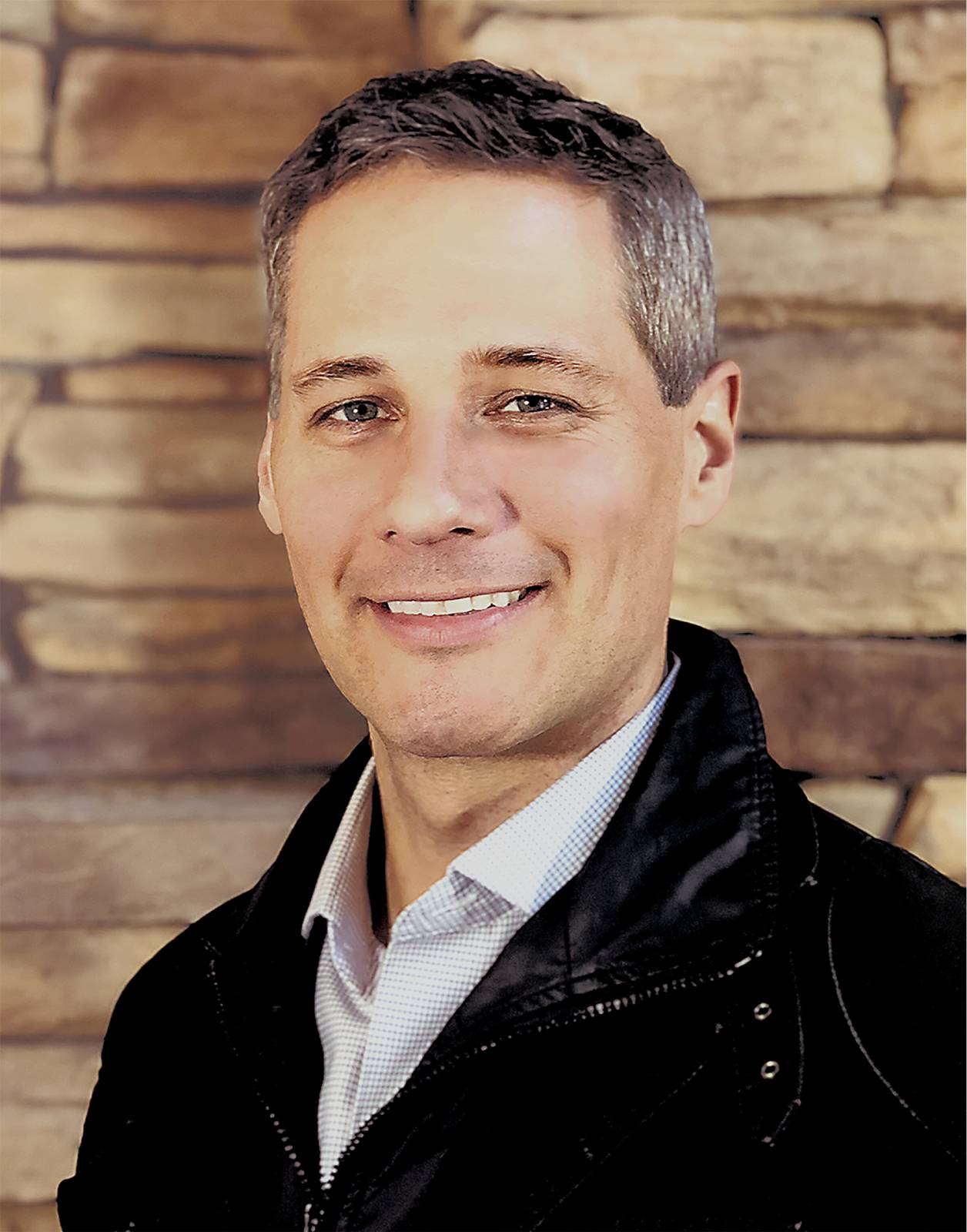 Head-and-shoulders portrait of a man smiling against a wooden backdrop.