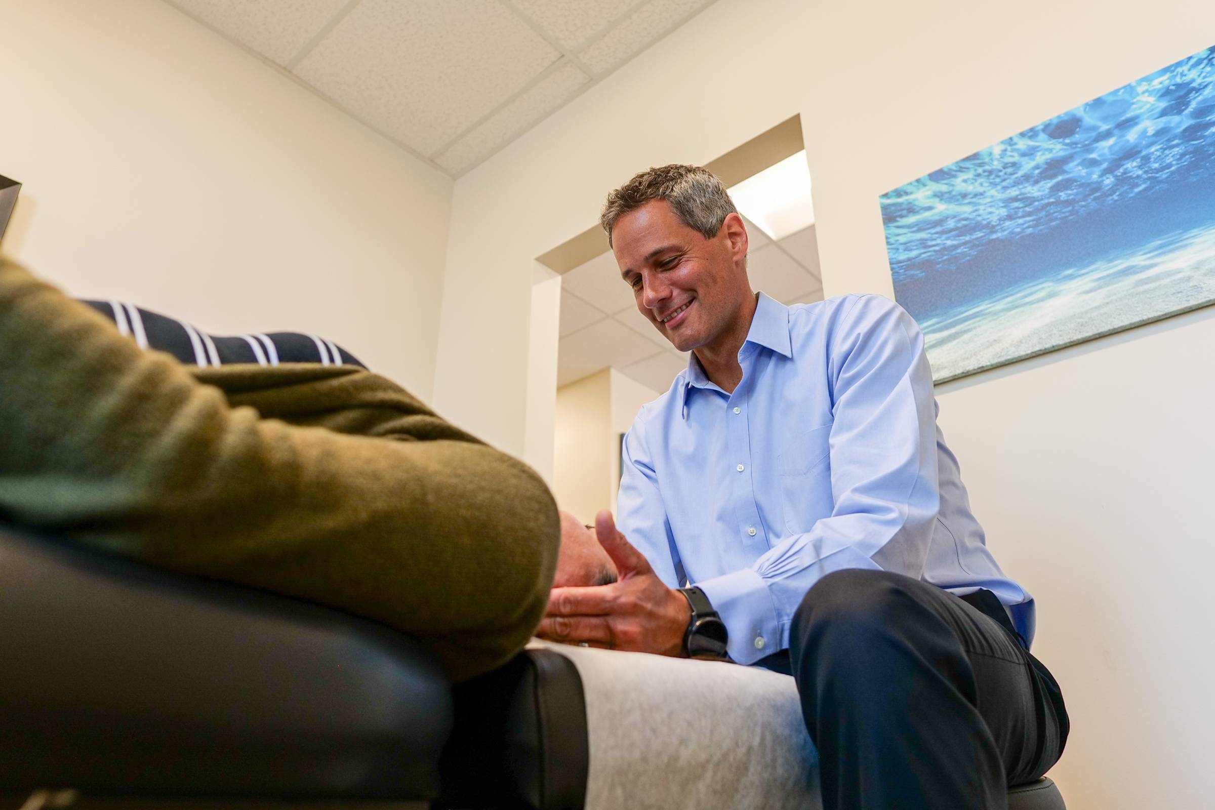 Chiropractor in blue shirt attends patient on exam table, smiling