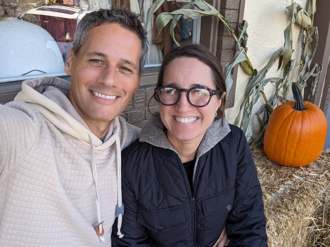 Smiling couple posing outdoors with a pumpkin.