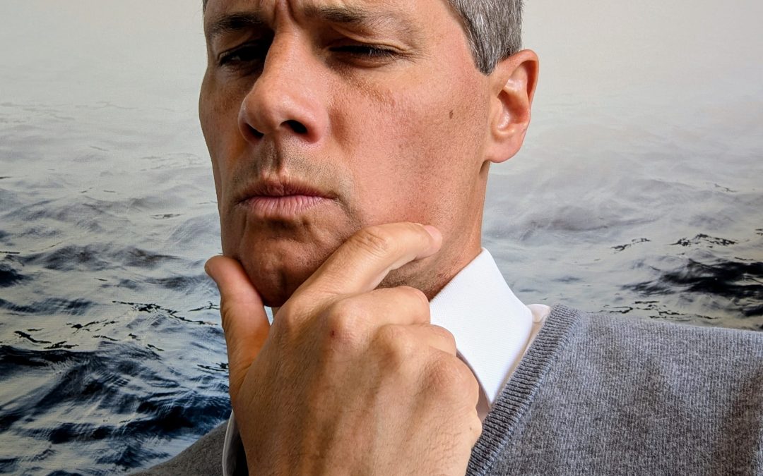Man in suit pondering with hand on chin, sea backdrop