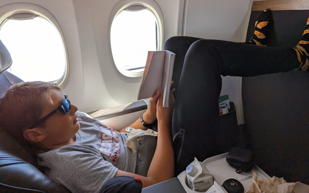 Boy wearing sunglasses reading a book on an airplane
