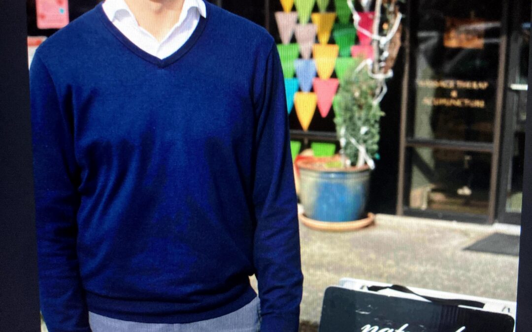 Person wearing a blue sweater standing outside a storefront with colorful bunting